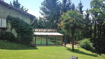 Un jardin avec une terrasse fermée par des baies vitrées, une pelouse et des arbres tout autour.