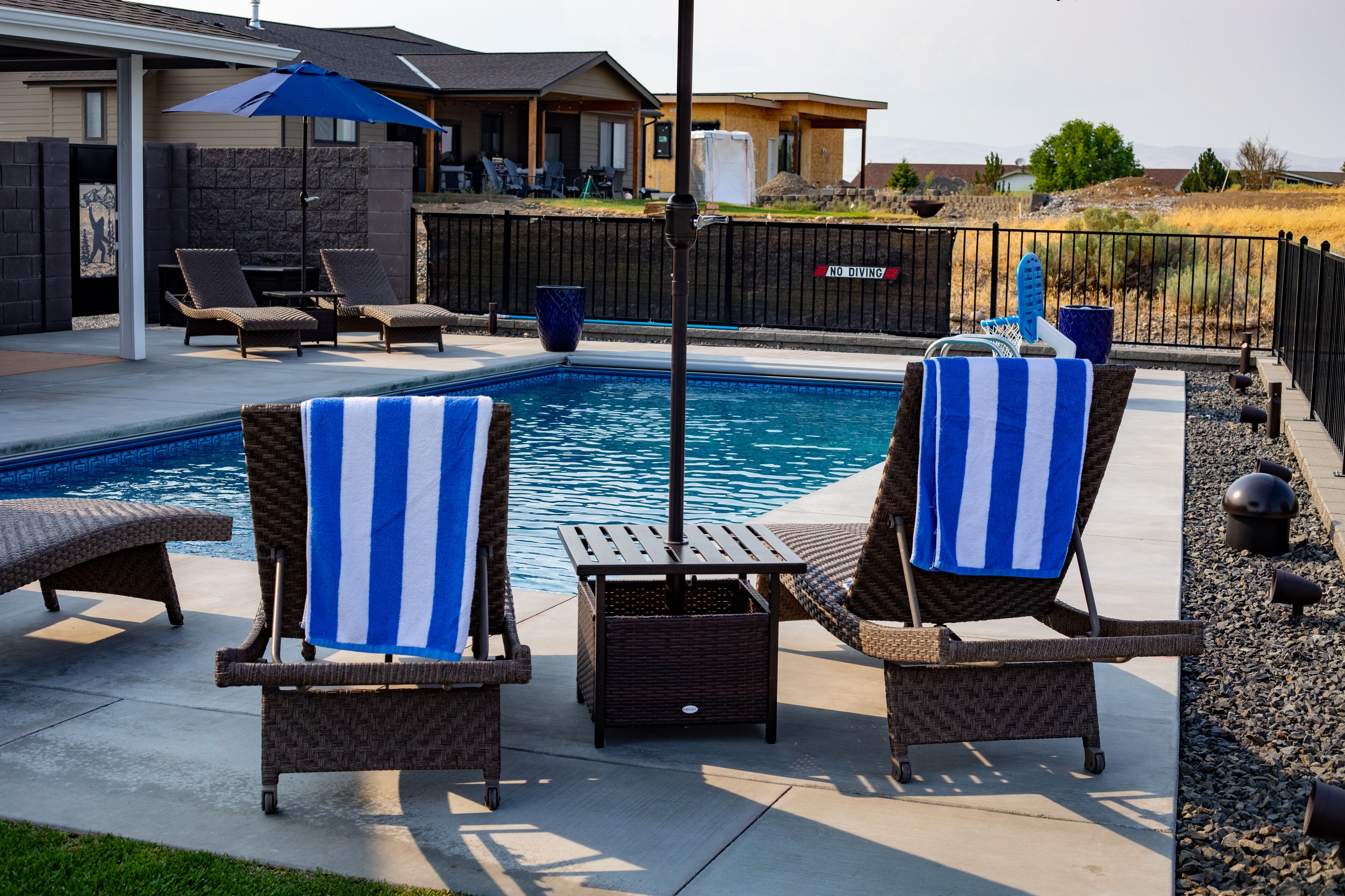 A backyard with a swimming pool, lounge chairs, and a patio umbrella.
