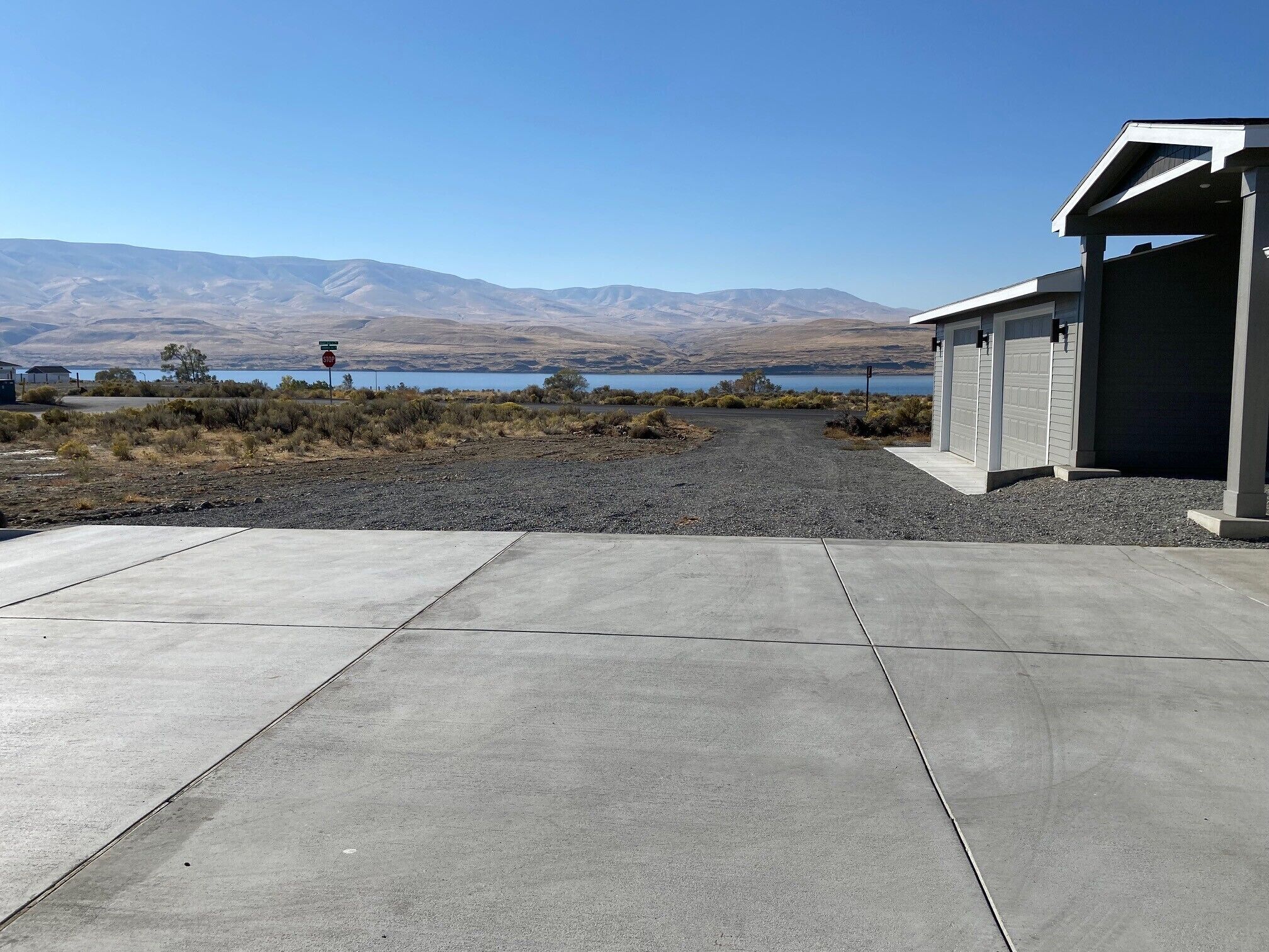 A concrete driveway leading to a building with a garage, a clear view of a lake and mountains in the background.