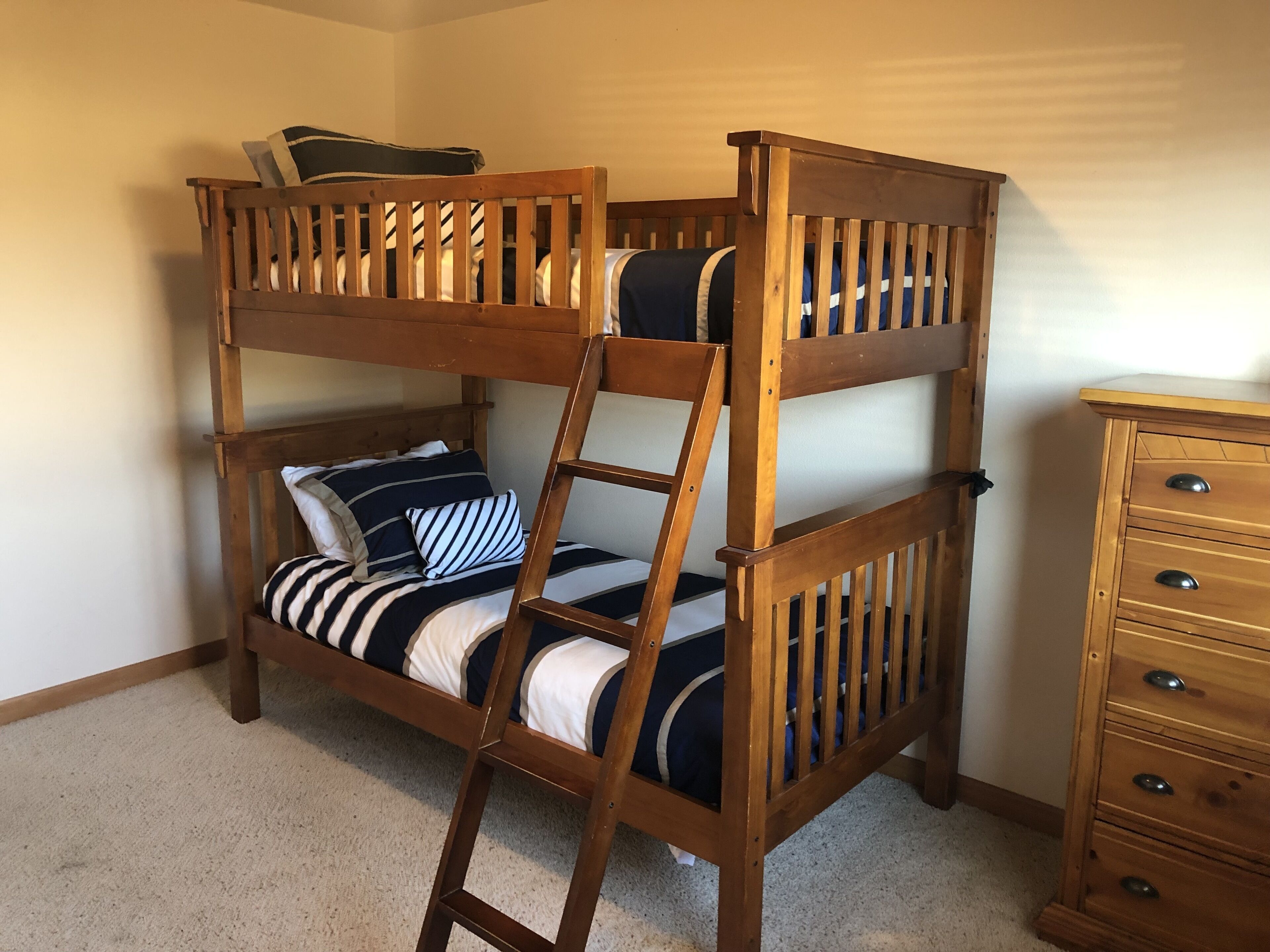 A bunk bed with a ladder, a dresser, and striped bedding.