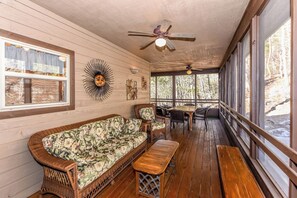 Eine gemütliche Holzterrasse mit einer Couch, Sesseln und einem Tisch, ausgestattet mit großen Fenstern und Deckenventilatoren.