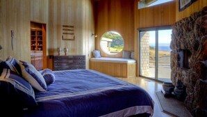 Quarto com uma cama grande, um banco embutido, parede de pedra e vista para o exterior.