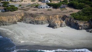 Uma área costeira com uma praia de areia, falésias rochosas e um morro arborizado.