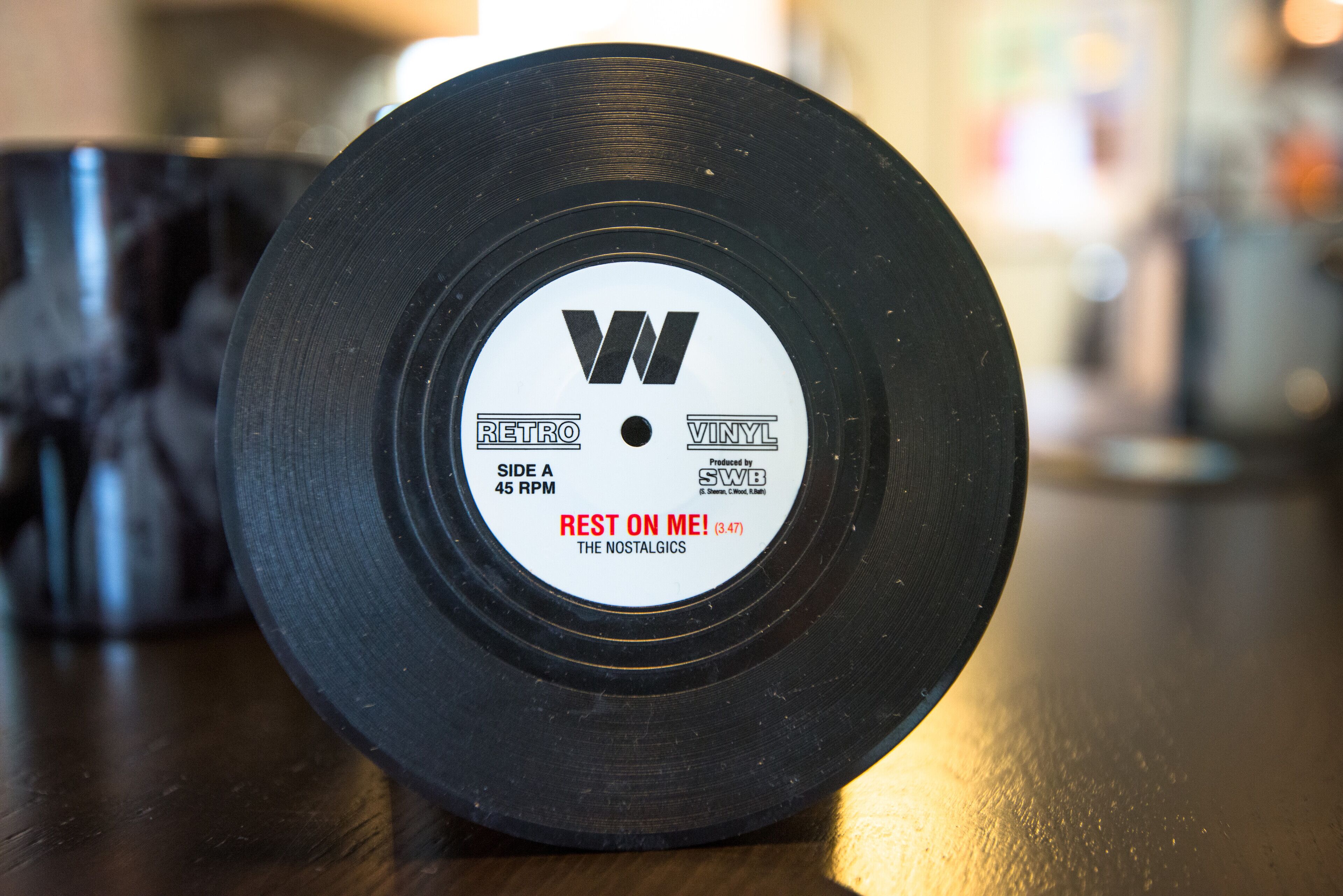 Un disco de vinilo con una etiqueta que indica que es un disco de 45 RPM, producido por SWB, y titulado 'REST ON ME!' de The Nostalgics.