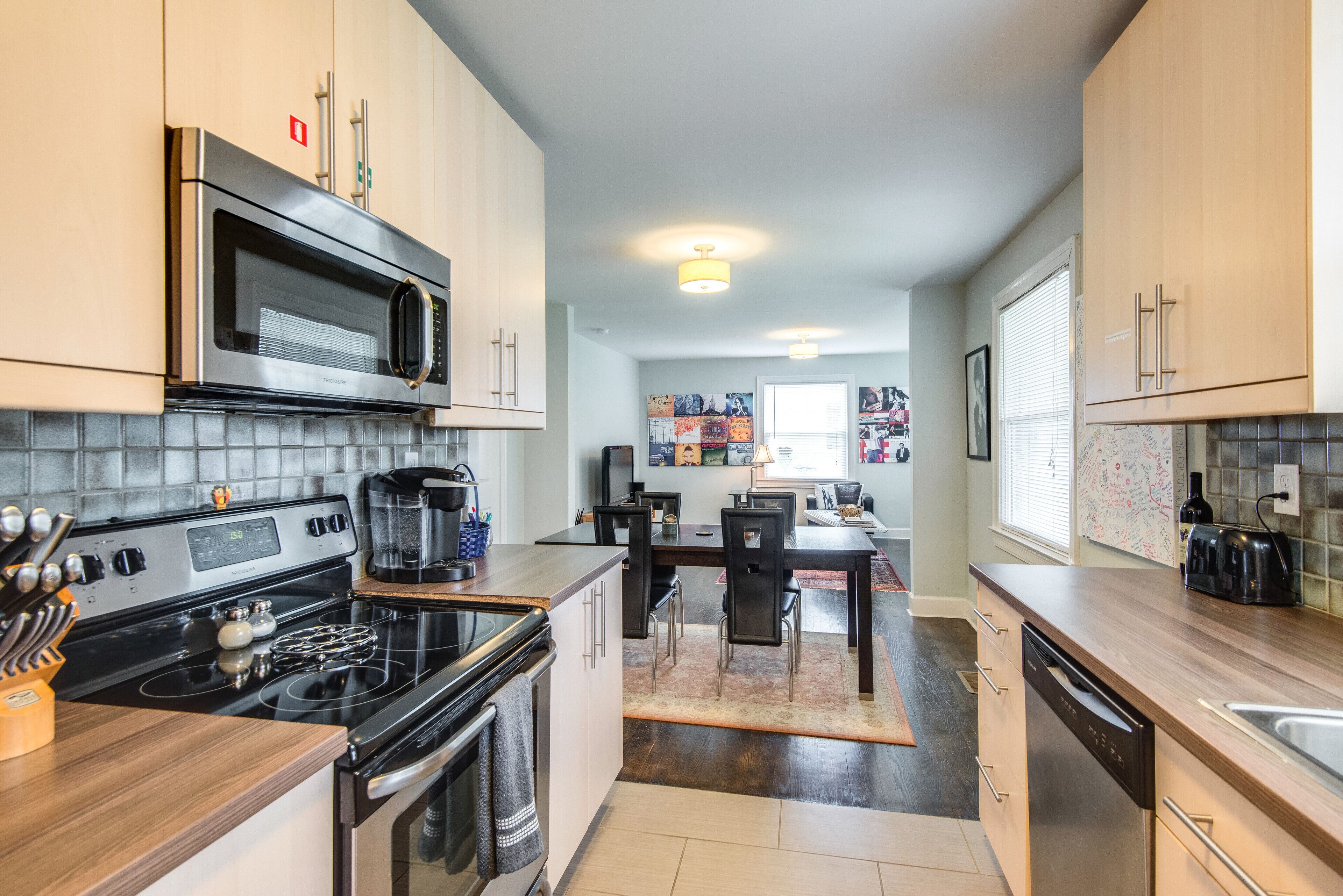 Cozinha moderna com eletrodomésticos de aço inoxidável, armários de madeira e um espaço de refeições com mesa e cadeiras.