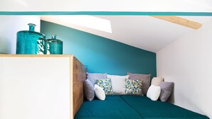 Una habitación acogedora, de forma triangular, con una pared color turquesa, un cabecero de madera y un tragaluz.