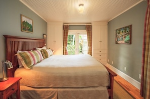 A bedroom with a large bed, a nightstand, a dresser, and a window with curtains. - Mango Haus - Savor Tropical Living by a Lush Lagoon Pool (West Palm Beach)