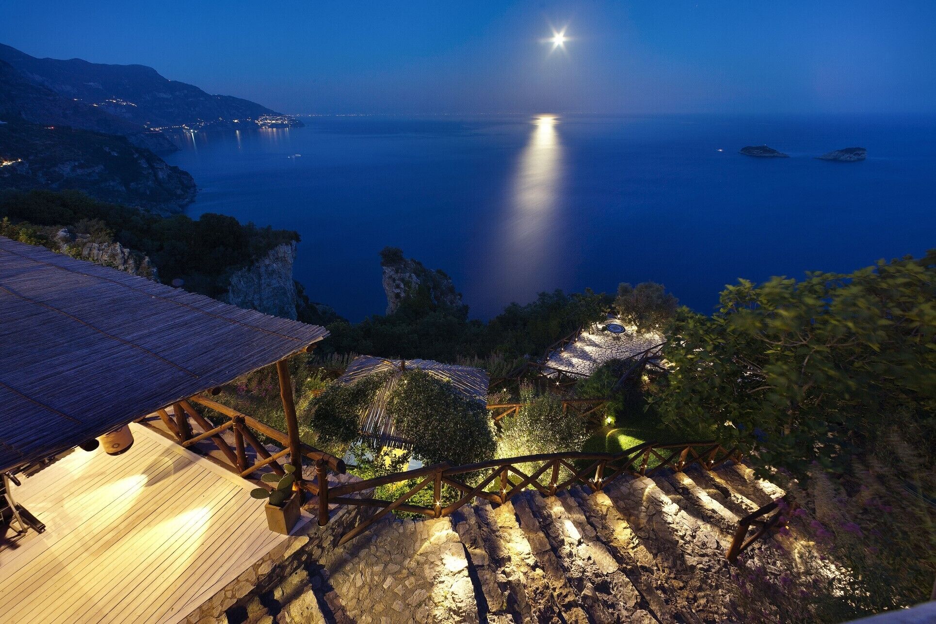 Une vue sur la côte de nuit, avec une terrasse en bois et des marches en pierre menant à un bâtiment dont le toit est recouvert de chaume.