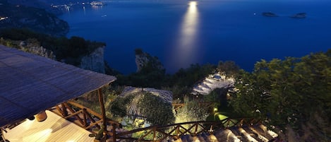 A coastal view at night with a wooden deck and stone steps leading to a building with a thatched roof.