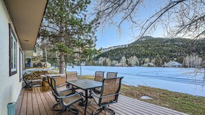 Een houten terras met een tafel en stoelen, met uitzicht op een meer en beboste heuvels.