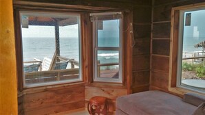 Eine Holzhütte mit einem großen Fenster zum Meer, einer Holzterrasse und einem kleinen Hocker.