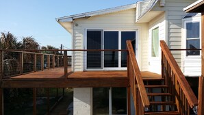 Eine Holzterrasse mit Geländer, eine Schiebetür und eine Treppe, die zu einem weißen Gebäude mit einem Fenster führt.