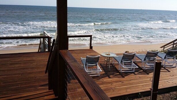 Eine Holzterrasse mit Liegestühlen und einem Tisch mit Blick auf das Meer.