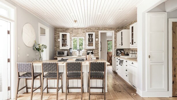 A kitchen with a central island, white cabinetry, and a brick accent wall.