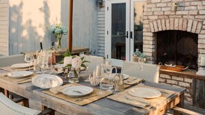 An outdoor dining area with a brick fireplace, a table set for four, and a white door in the background.