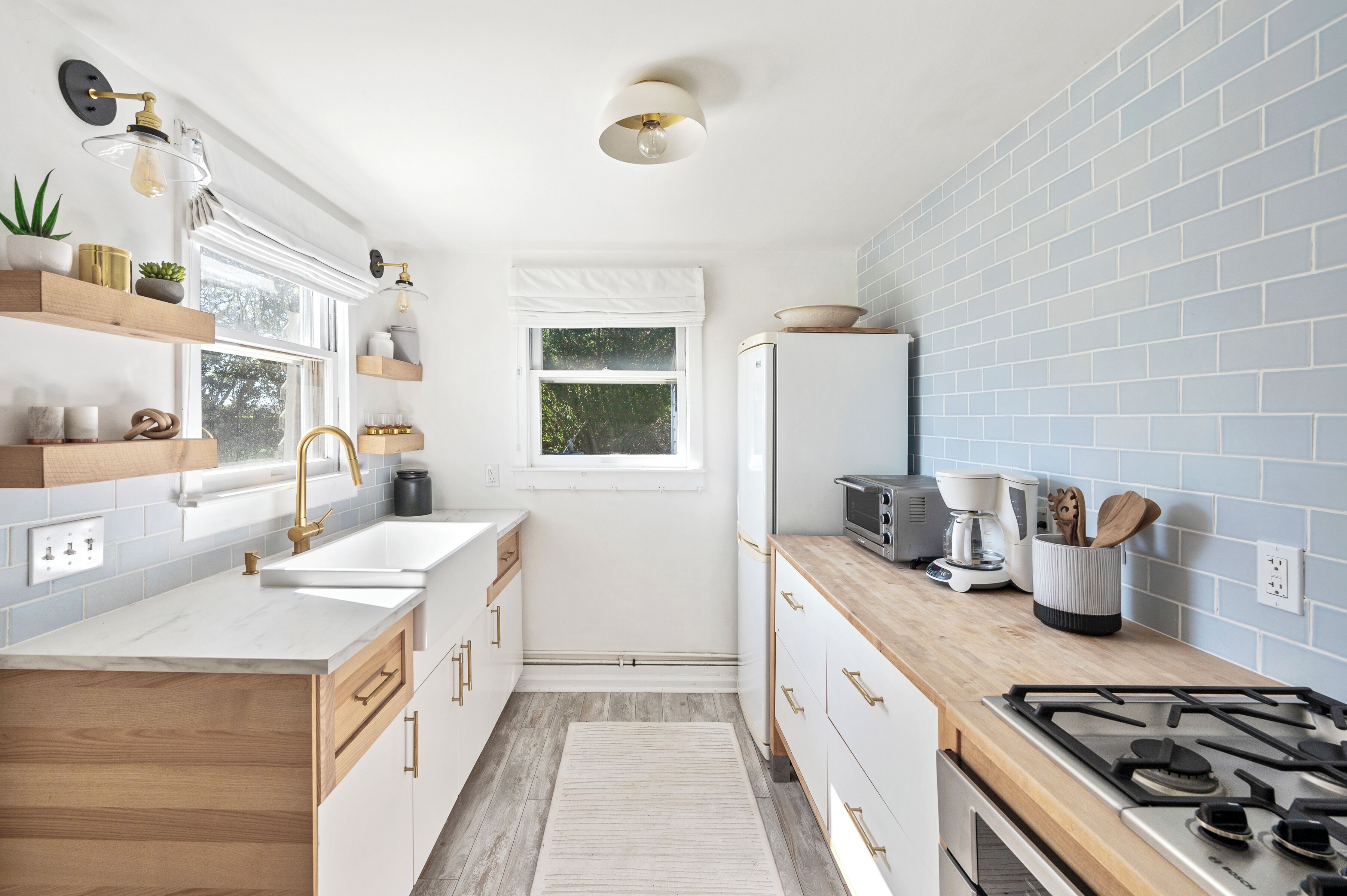 Une cuisine moderne avec des meubles blancs, un plan de travail en bois, une cuisinière à gaz et un four encastré. Une fenêtre offre une vue sur la verdure à l’extérieur.