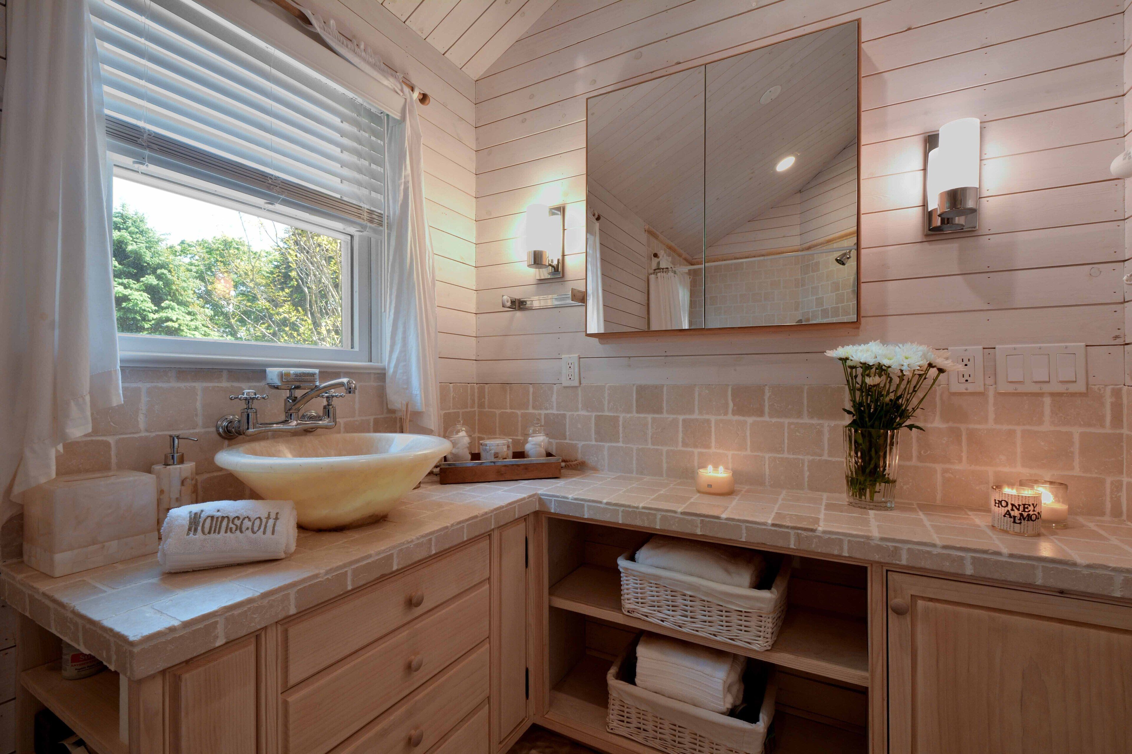 A bathroom with a large sink, a mirror, and a window with blinds. There are towels and a candle on the counter.