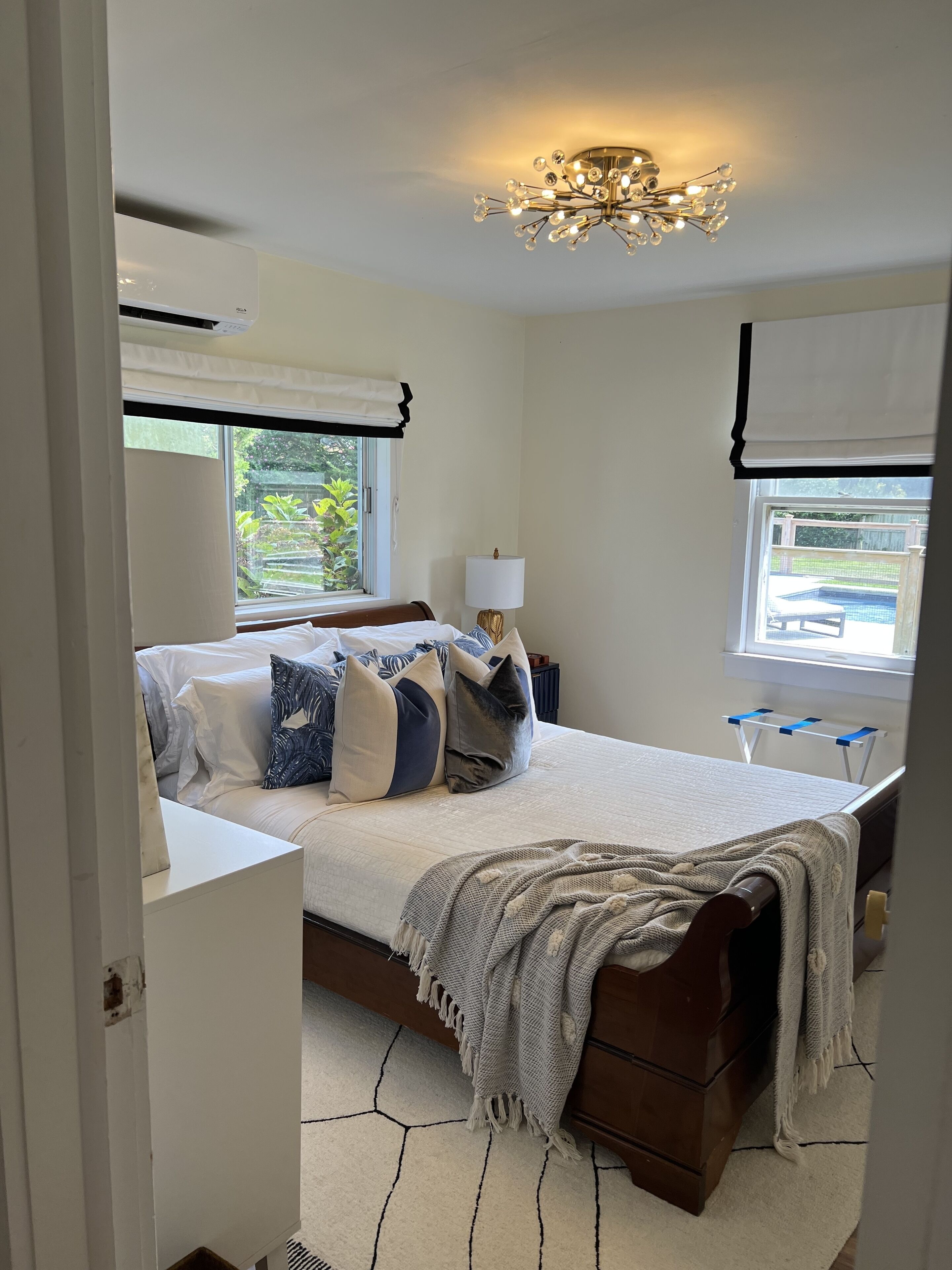 A bedroom with a large bed, bedside tables, a chandelier, and a window with a view of a pool.