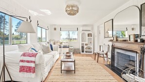 A spacious living room with a white fireplace, a large mirror, and a view of the outdoors.