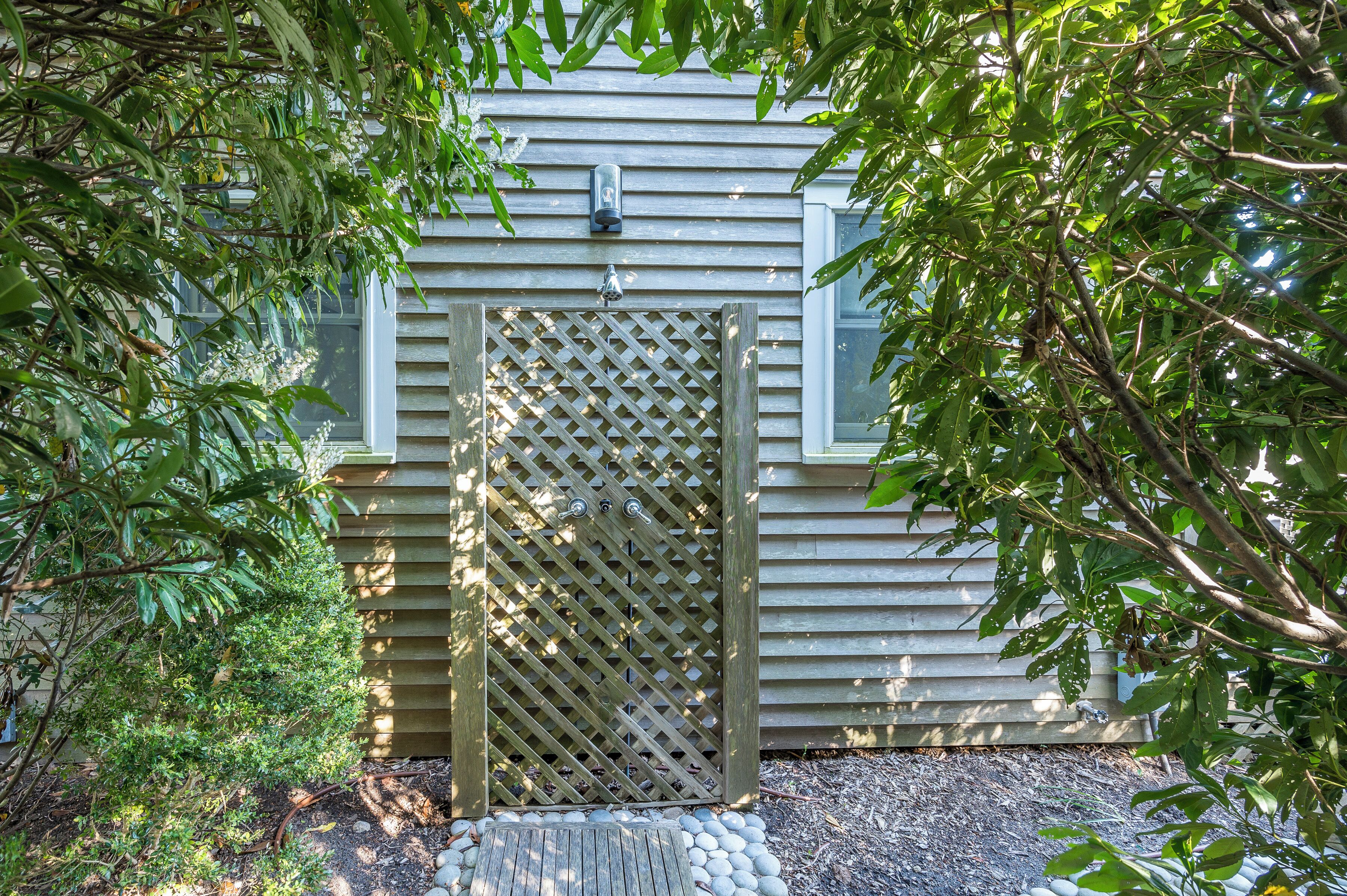 A wooden gate with a lattice design, leading to a building with horizontal siding.