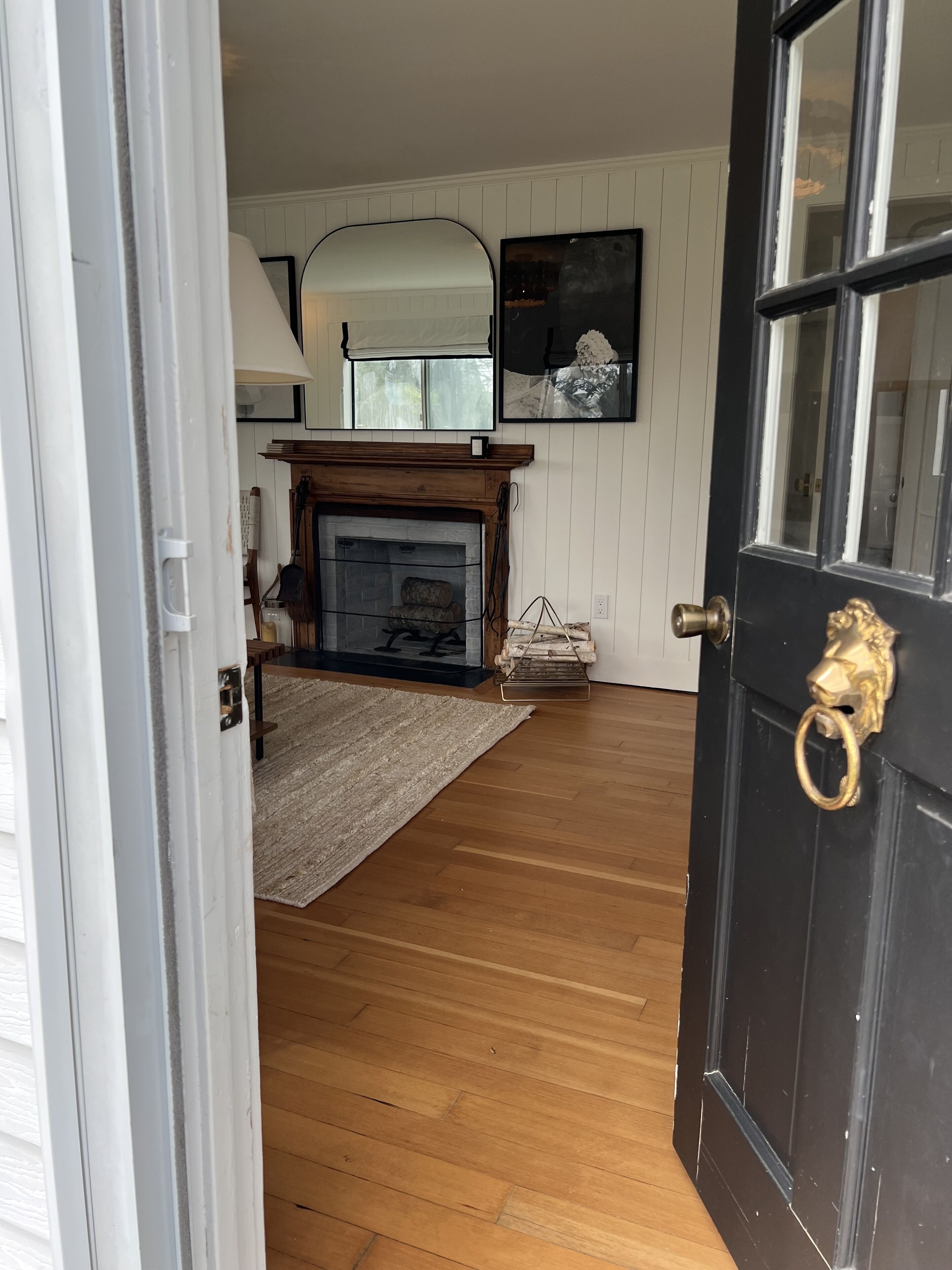 A room with a wooden floor, a fireplace, a rug, and a door with a brass handle.