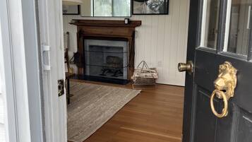 A room with a wooden floor, a fireplace, a rug, and a door with a brass handle.