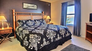 Une chambre à coucher avec un grand lit, deux tables de chevet avec des lampes, un ventilateur de plafond et une fenêtre avec des rideaux.