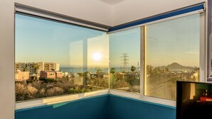 Ein Zimmer mit einem großen Fenster und Blick auf eine Küstenstadt, einem Fernseher und einer kleinen Sitzecke.