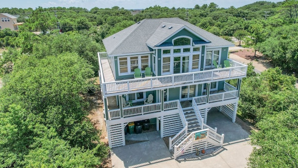 A two-story house with a balcony, surrounded by dense greenery. - 8 BEDROOMS: Book your vacation now! (Corolla)