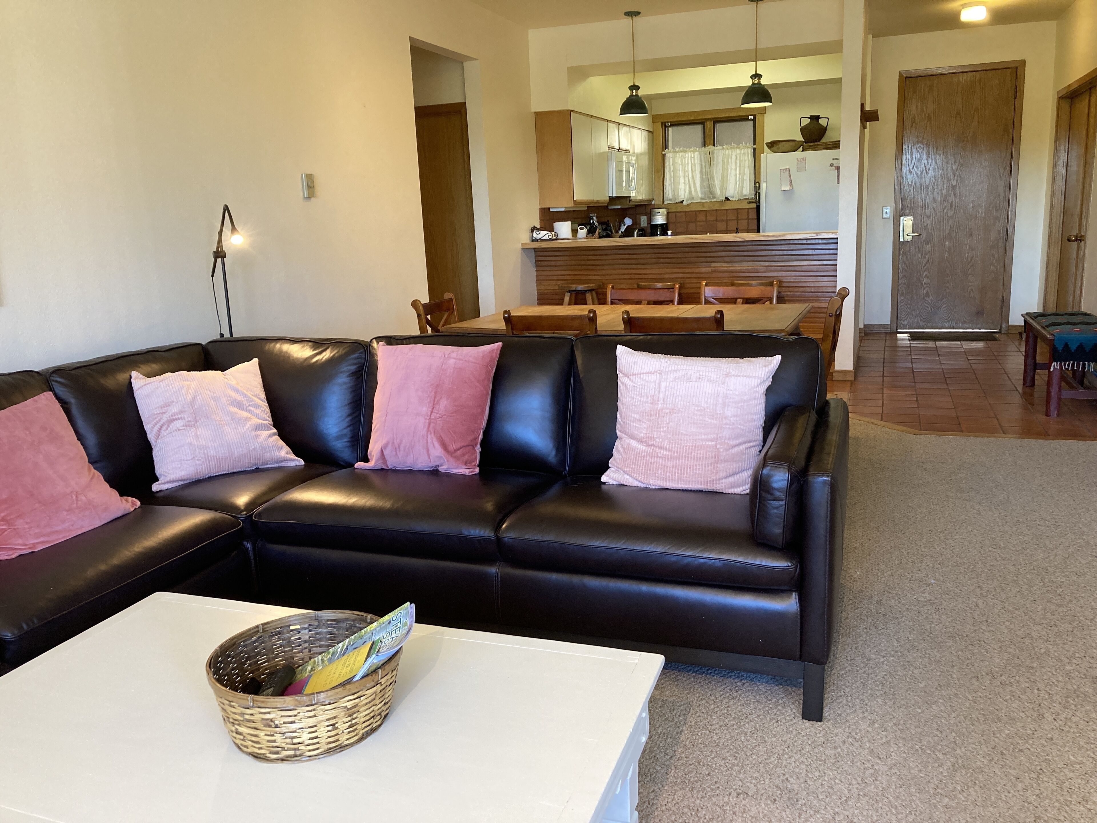 A living room with a black leather sofa, a white coffee table, and a wicker basket.