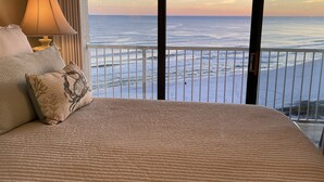 A bedroom with a large bed, a nightstand, a lamp, and a view of the ocean. - EXTREME MAKEOVER- 200 5 STAR REVIEWS. DIRECT BEACH VIEWS-LUXURY AT GREAT PRICING (Orange Beach)
