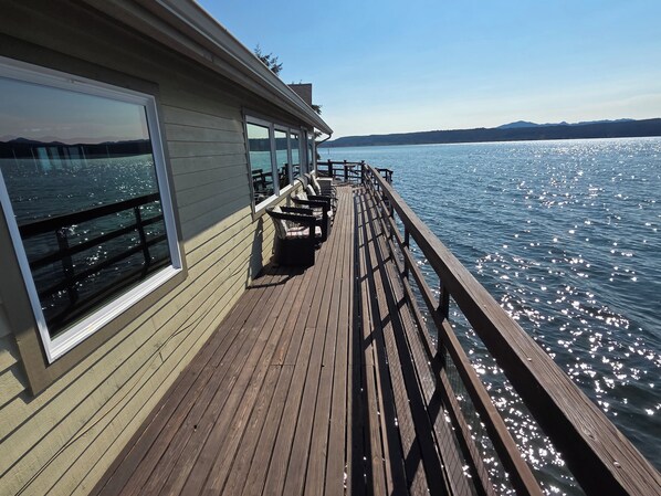 A wooden deck with a railing overlooking a body of water, a clear sky, and distant mountains.