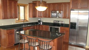 A kitchen with wooden cabinets, a stainless steel refrigerator, a built-in oven, and a bar stool area.