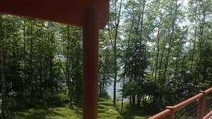 A wooden deck with a railing overlooking a grassy area and a forested area with a body of water in the background.