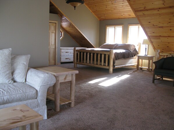 A cozy attic bedroom with a sloped ceiling, a wooden bed, a small table, a chair, and a sofa.