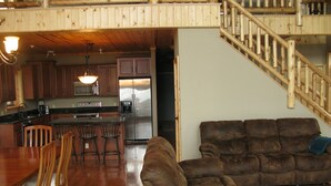 A spacious living area with a wooden floor, a brown sofa, a dining table with chairs, and a kitchen in the background.