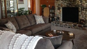 A cozy living room with a stone fireplace, a wooden staircase, and a comfortable sofa set.