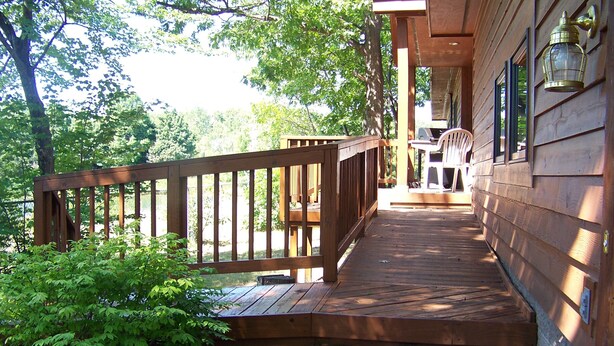 A wooden deck with a railing, a barbecue grill, and a lantern on the wall.