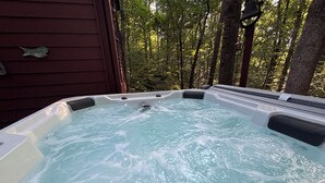 Un bain à remous avec une terrasse en bois et une forêt en arrière-plan.