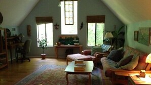 Un salon confortable avec un plafond haut, un canapé, une table basse, un bureau et une fenêtre avec des stores.