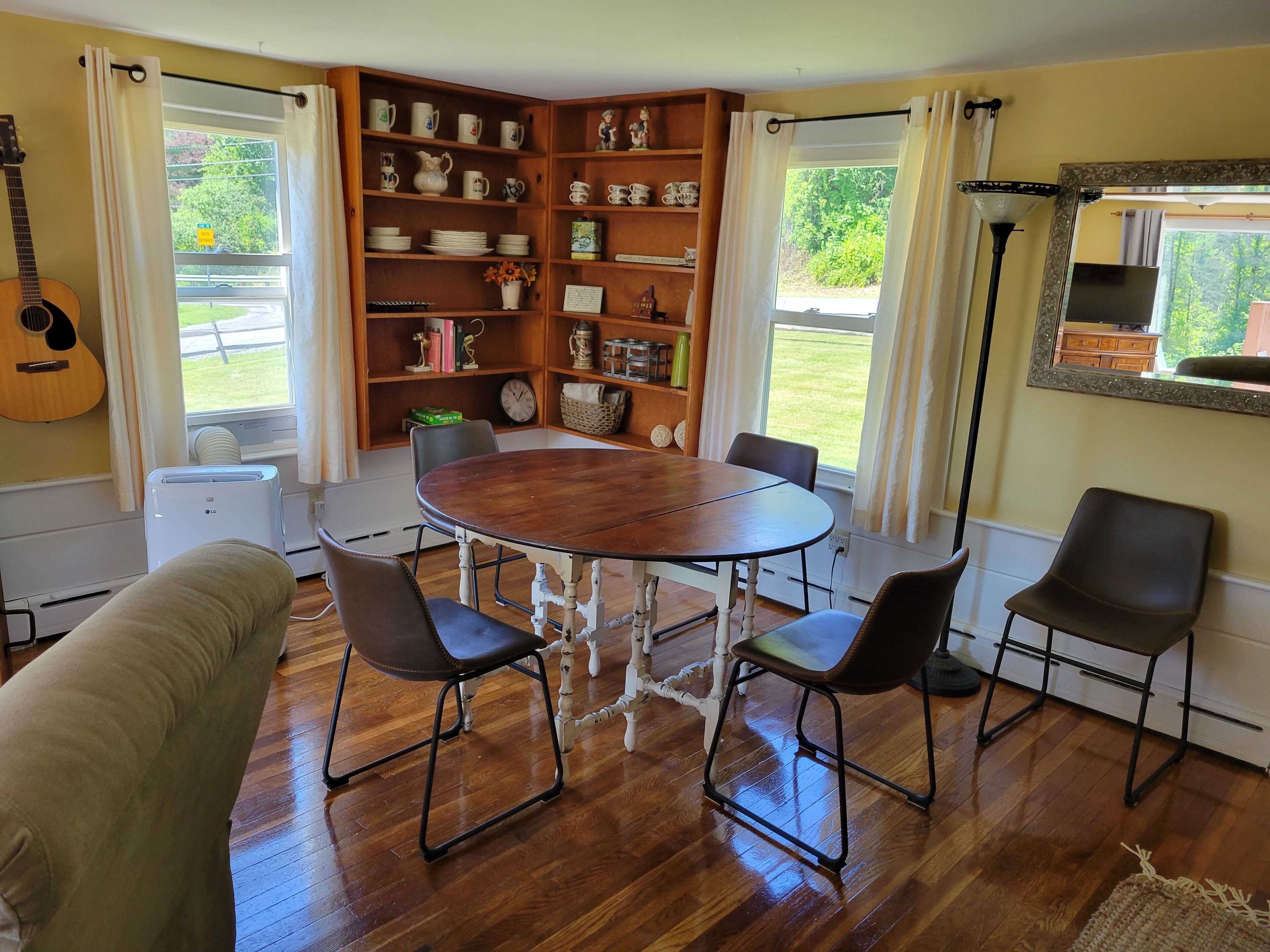 Un comedor con una mesa de madera, cuatro sillas, una estantería y una guitarra.