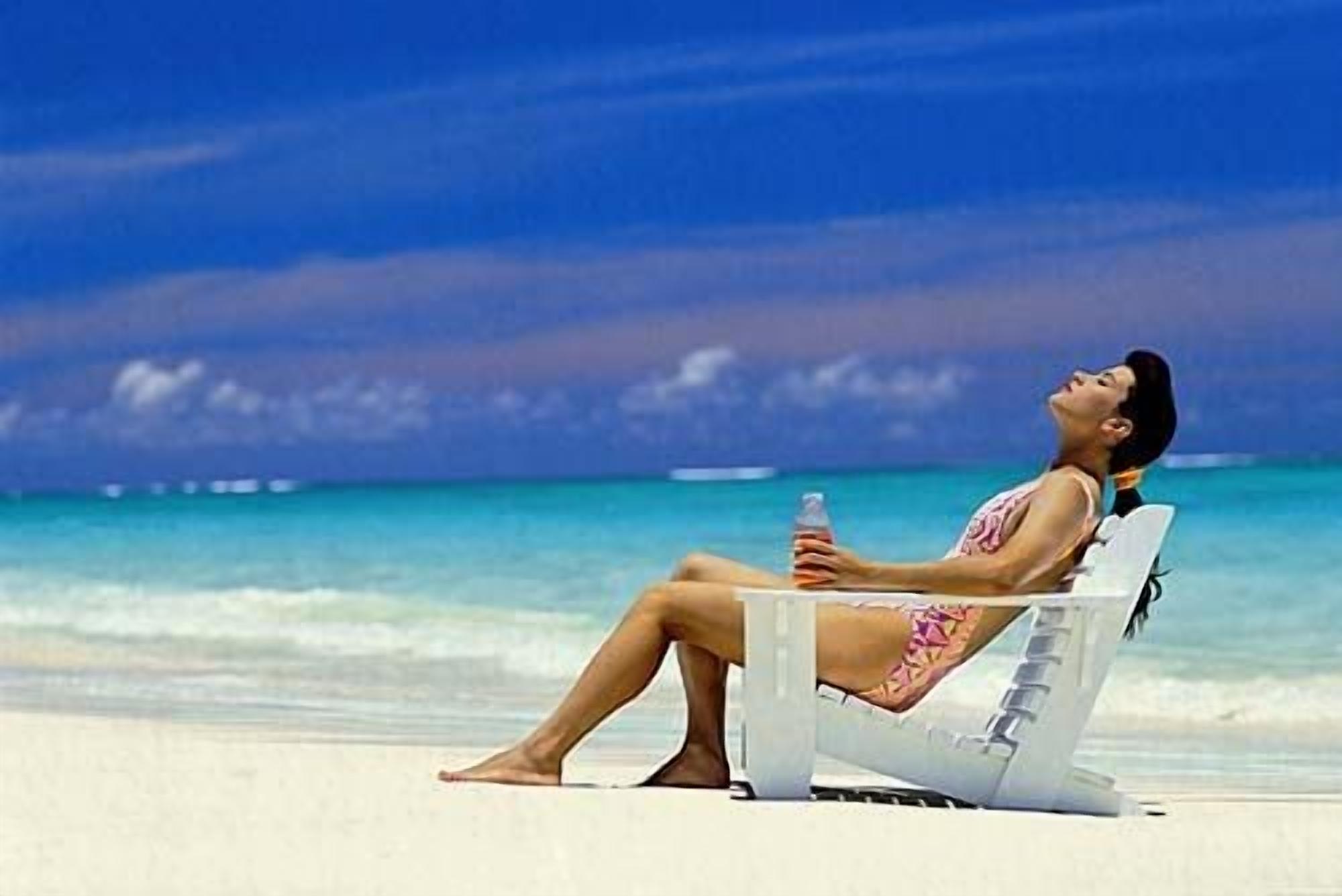 Eine Person entspannt sich in einem Liegestuhl am Strand, mit einer Flasche, mit Blick auf das Meer.