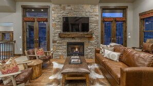 Una sala de estar acogedora con chimenea de piedra, muebles de cuero y un televisor grande.