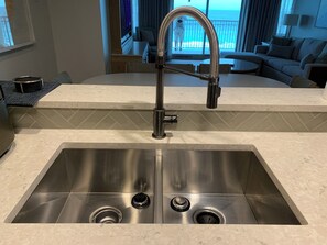 Una cocina moderna con un lavamanos de acero inoxidable, un grifo curvo y vista al océano a través de la ventana.