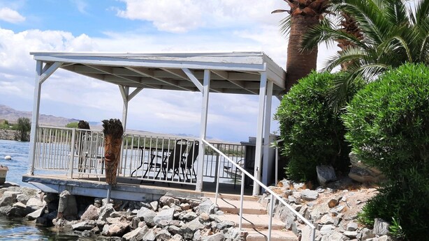 A covered outdoor seating area with metal railings and a stone pathway leading to a body of water. - WATERFRONT,PRIVATE BOAT RAMP ,SANDY BEACH GATED COMMUNITY, 3 BEDROOM & 2 BATH (Mohave Valley)
