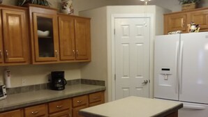 A kitchen with wooden cabinets, a white refrigerator, and a blue trash bin. - WATERFRONT,PRIVATE BOAT RAMP ,SANDY BEACH GATED COMMUNITY, 3 BEDROOM & 2 BATH (Mohave Valley)