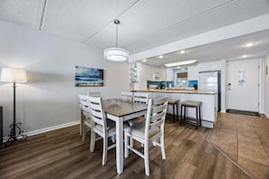 A modern kitchen with white cabinets, a central island, and a dining area with a wooden table and chairs.