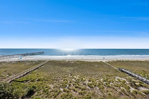 A beach with a wooden pier extending into the ocean, a sandy beach, and grassy dunes.