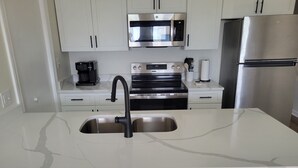 A modern kitchen with a double sink, stainless steel appliances, and white cabinetry. - Surfside Beach Paradise! Steps to the Beach, Ocean View, Family Friendly (Surfside Beach)