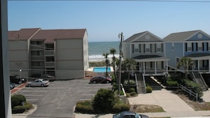 A coastal view with a parking lot, a swimming pool, and buildings with balconies overlooking the ocean. - Surfside Beach Paradise! Steps to the Beach, Ocean View, Family Friendly (Surfside Beach)